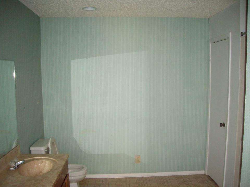 Bathroom with sink, toilet, and door. Light green striped wallpaper