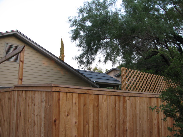 Wooden fence in front of a house with trees and a lattice section