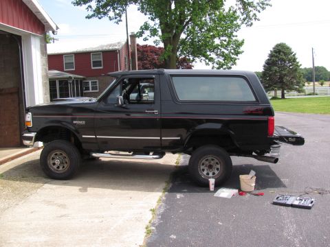 1995 Ford Bronco - A black Ford Bronco is parked next to a garage with its tailgate open, and tools are laid out on the asphalt.