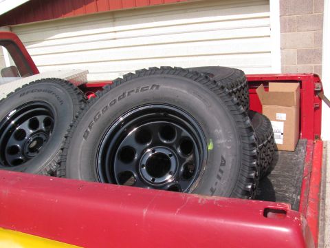 1995 Ford Bronco - Spare BFGoodrich All-Terrain tires and black rims are stored in the bed of a red truck.