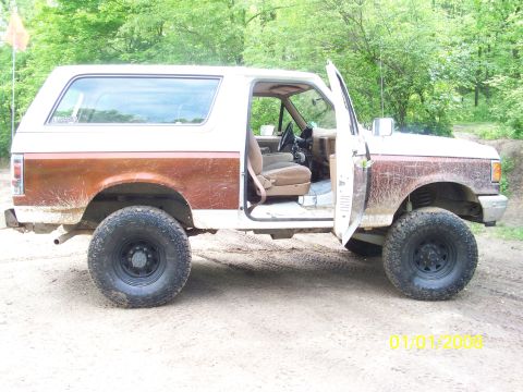 1989 Ford Bronco - This 1989 Ford Bronco is shown with its driver's side door open, parked outdoors on a dirt path.