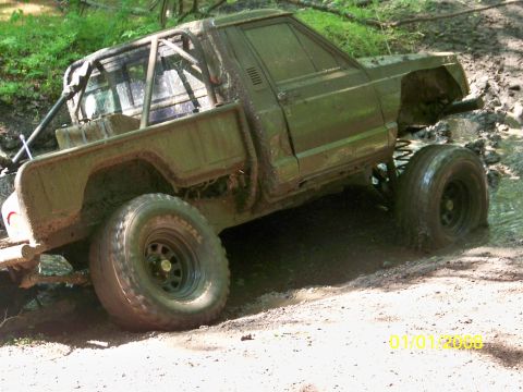 1989 Ford Bronco - A heavily modified, mud-caked pickup truck navigates a challenging off-road terrain.