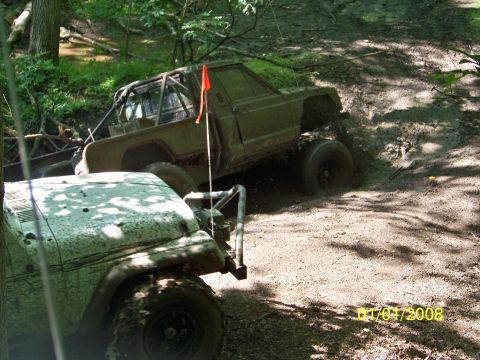 1989 Ford Bronco - Two off-road vehicles tackle a challenging muddy terrain, one equipped with a protective roll cage.