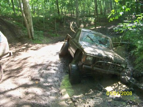 1989 Ford Bronco - This Jeep is deep in the mud on a wooded trail, with another vehicle nearby.