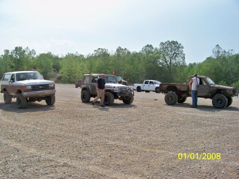 1989 Ford Bronco - A lifted 1989 Ford Bronco is parked on a gravel lot with other off-road vehicles.