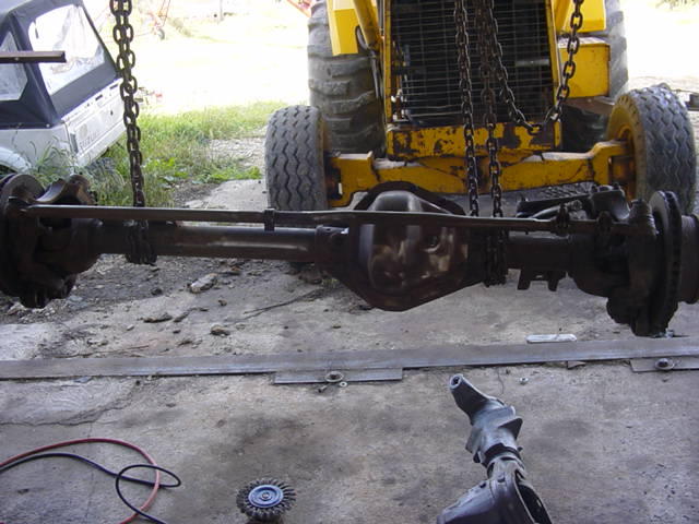 Differential and axle assembly hanging from chains, with a yellow loader in the background