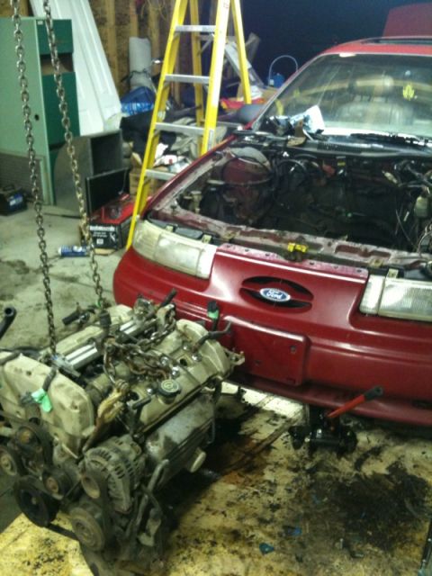 1990 Ford Probe - A red car sits in a garage with its engine removed, ready for repair or replacement.