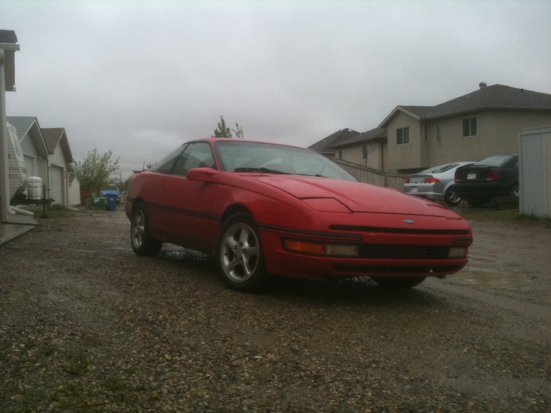 Red Ford Probe coupe with aftermarket wheels parked in residential driveway