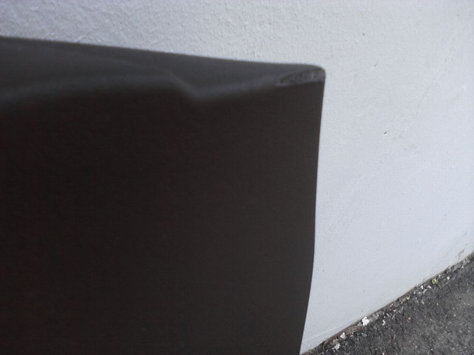 Close-up of a dark, textured car part against a white wall