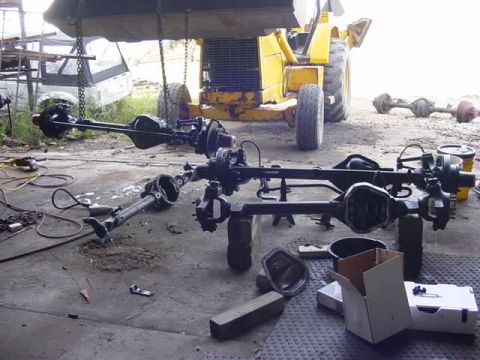 1992 Ford Bronco - Vehicle axles and parts are disassembled and arranged on the ground, with heavy machinery visible behind.