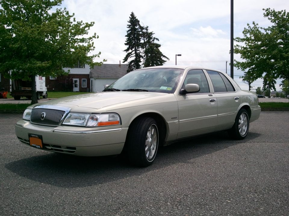 Gold four-door sedan parked on asphalt, front three-quarter view with chrome grille and alloy wheels