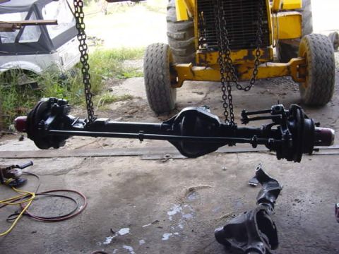 1992 Ford Bronco - A rear axle assembly is suspended by chains, with a yellow tractor and another vehicle part visible in the background.