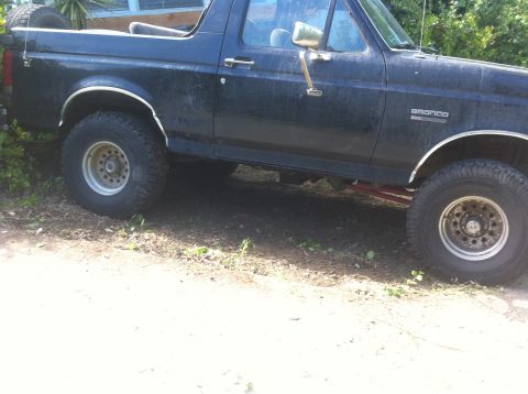 1990 Ford Bronco - A dark blue Ford Bronco is parked outdoors, with visible chrome accents and off-road tires.