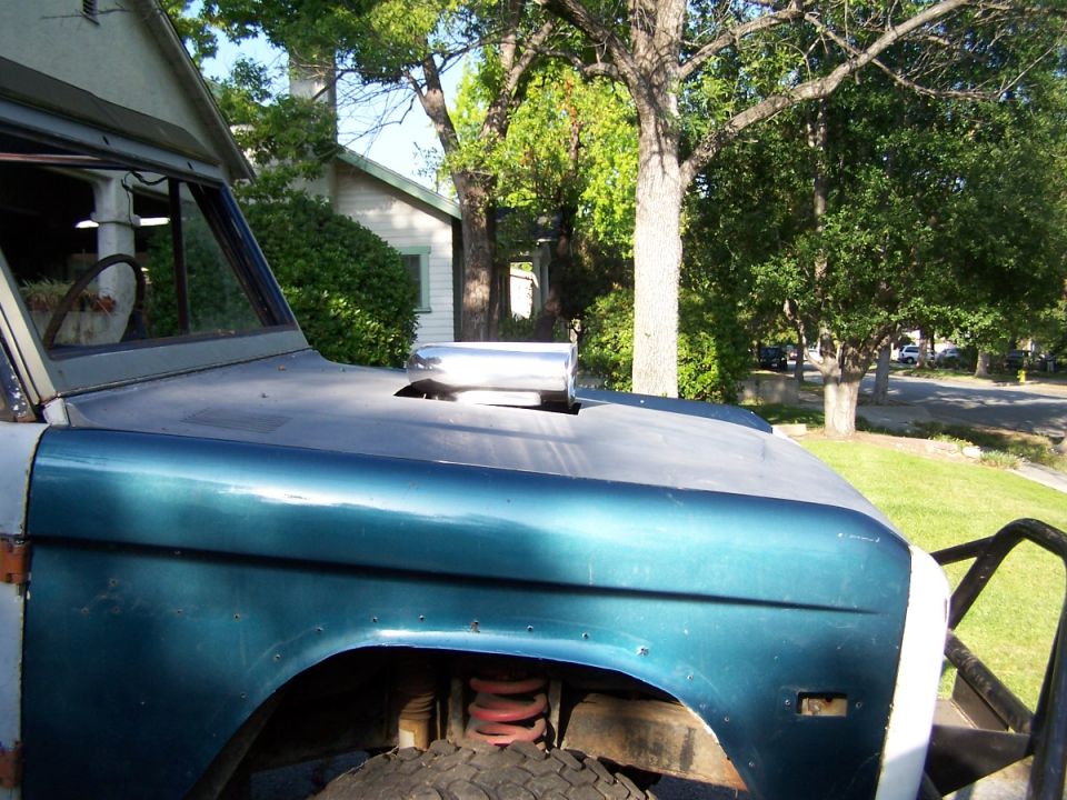 Side view of a teal and gray Ford Bronco with a chrome hood scoop. Off-road bumper visible