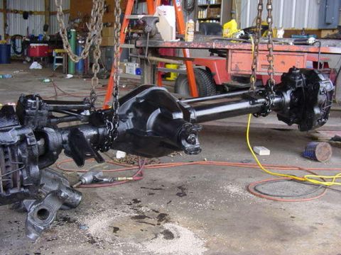 1992 Ford Bronco - A vehicle's front axle assembly is suspended by chains, ready for installation or repair.