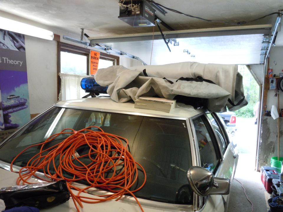 Car in garage with blue lights on roof, covered items, and orange cord on windshield