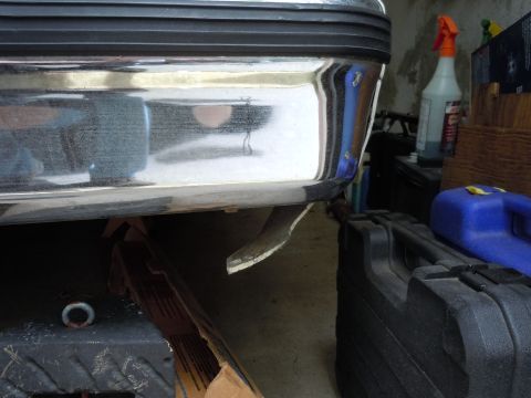 2001 Ford Crown Victoria - Close-up of a chrome rear bumper and exhaust pipe, with storage cases and cleaning supplies in the background.