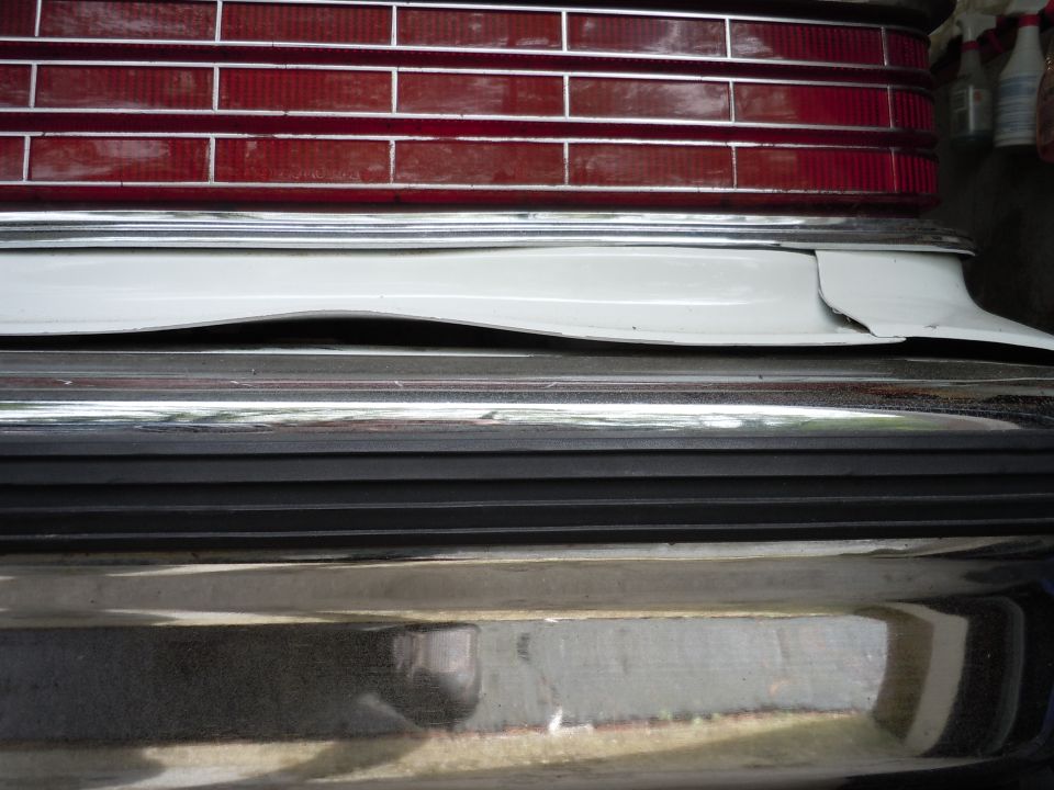 Rear bumper and taillight of a white vehicle with chrome trim and a damaged white panel