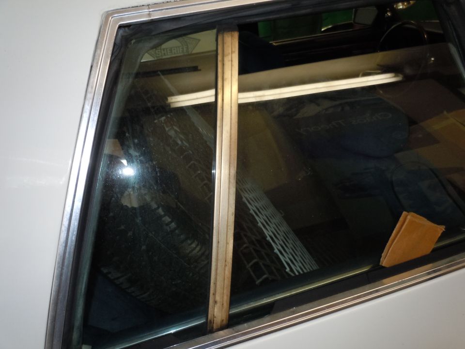 Interior of a white car showing a wooden trim piece and a reflection of a sheriff's badge