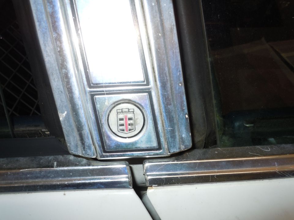 Chrome trim piece with a circular crest emblem showing red and white stripes, on a white vehicle