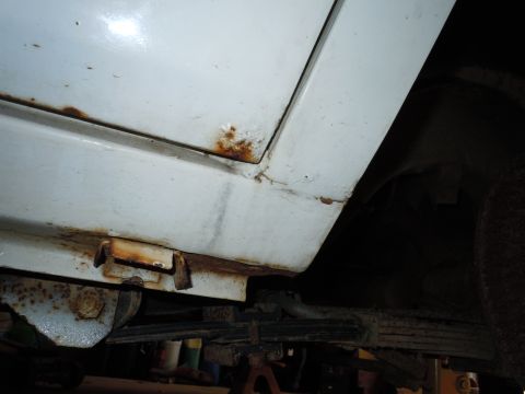 2001 Ford Crown Victoria - Close-up view of the lower body panel of a white vehicle, revealing significant rust and visible suspension parts underneath.
