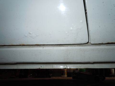 2001 Ford Crown Victoria - Close-up view of a white car's door seam and rocker panel, showing signs of rust.