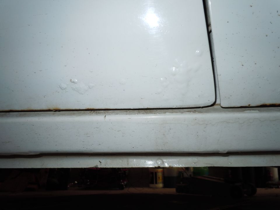 close-up of white car door seam and rocker panel with rust spots