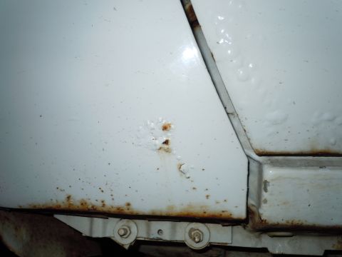 2001 Ford Crown Victoria - Close-up view of rust and corrosion on a white vehicle's lower body panel, indicating poor condition.