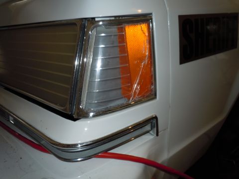 2001 Ford Crown Victoria - The front corner of a white vehicle, possibly a police car, with a cracked turn signal and "SHERIFF" text visible.