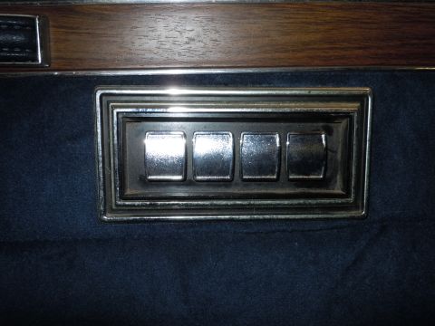 2001 Ford Crown Victoria - Interior view of power window controls on a car door panel, showing four switches.