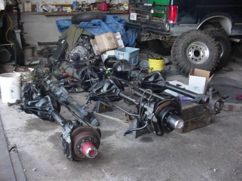 1992 Ford Bronco - A collection of vehicle axles and engine components are stored in a workshop, with a truck visible in the background.