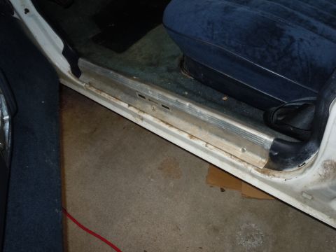 2001 Ford Crown Victoria - Close-up view of a car's interior door sill, showing the blue seat and weathered metal trim.
