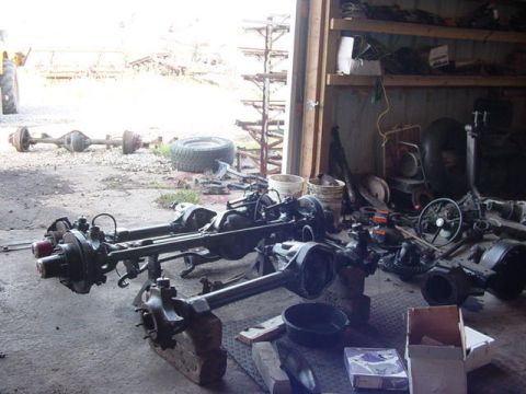 1992 Ford Bronco - Various vehicle axles are stored and displayed in a cluttered workshop environment.
