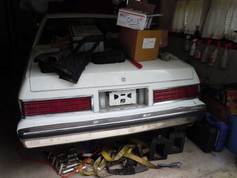 2001 Ford Crown Victoria - The rear of a white sedan is shown, with items piled on its trunk and straps underneath.