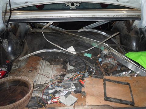 2001 Ford Crown Victoria - The trunk of a vehicle is cluttered with various items, including electrical wiring, metal trim pieces, and other assorted debris.