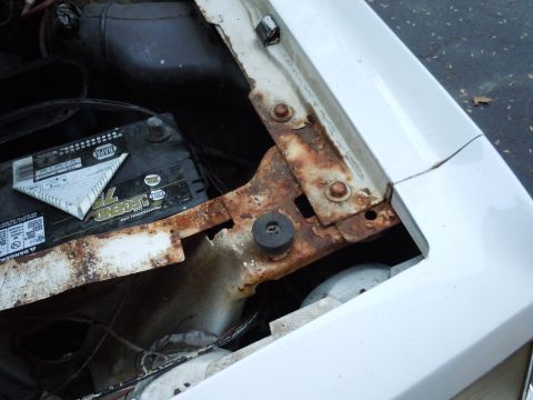 2001 Ford Crown Victoria - The engine bay of a white car displays significant rust around the battery tray and mounting points.