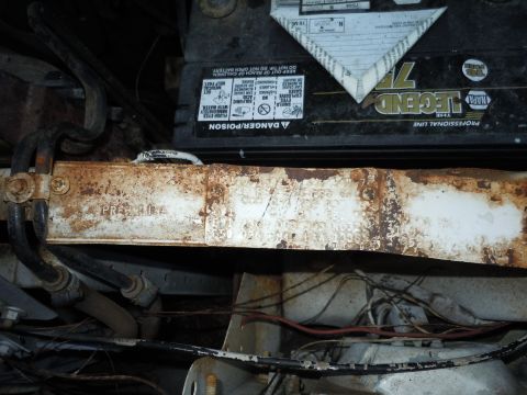 2001 Ford Crown Victoria - Close-up of a car battery and a heavily rusted metal component, likely from an engine bay.
