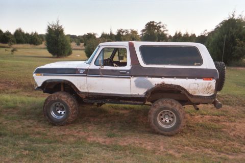 1978 Ford Bronco - Lifted 1978 Ford Bronco with large off-road tires sits in a muddy field.