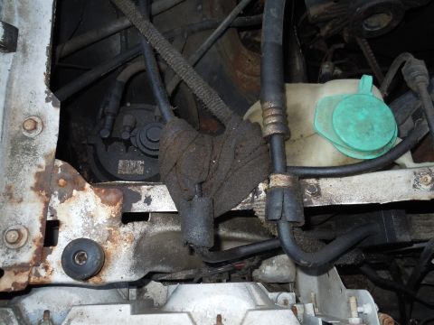 2001 Ford Crown Victoria - Close-up view of various engine bay components, including hoses and a coolant reservoir, with visible signs of rust.