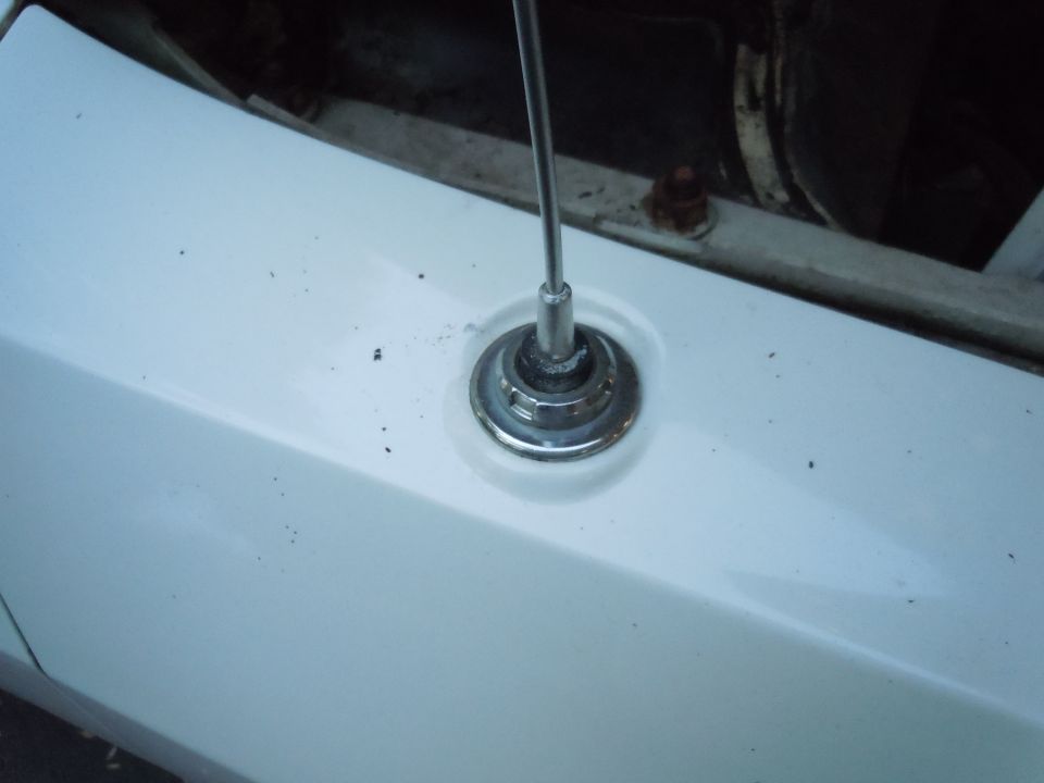 Chrome antenna base on white car fender, showing some dirt and rust