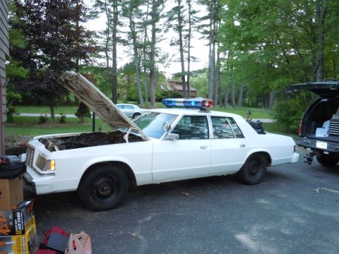 2001 Ford Crown Victoria - This white police car, seen from the side with its hood open and light bar illuminated, appears to be a model from the 1980s, not a 2001 Fo…
