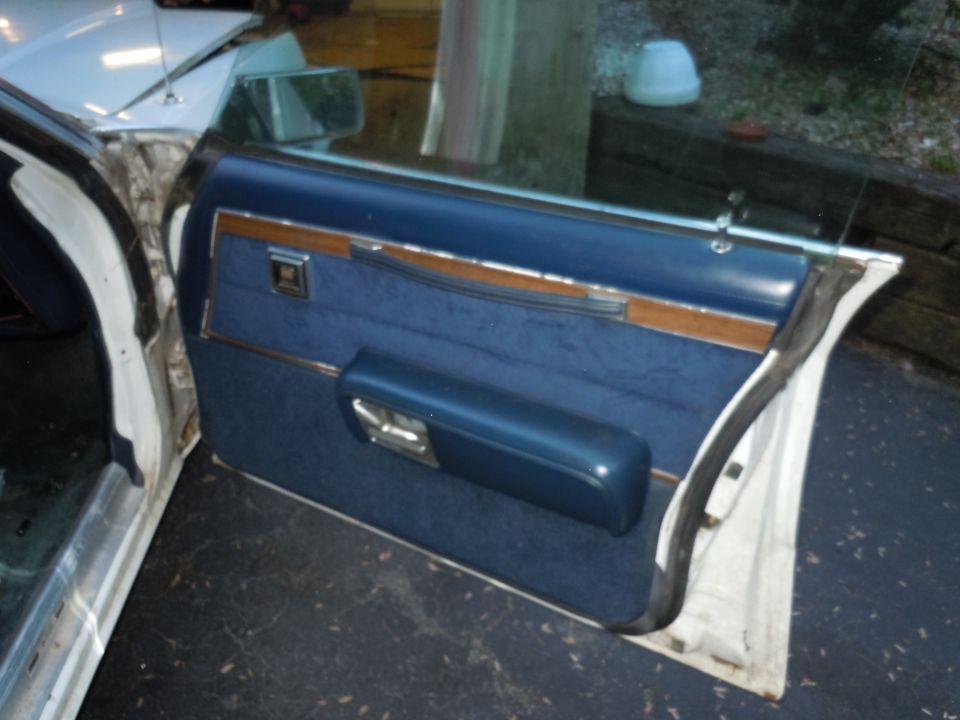 Car door panel with blue fabric, wood trim, and a blue armrest. The door is open, revealing the interior frame