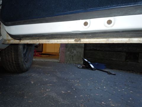 2001 Ford Crown Victoria - Lower section of a vehicle's door and a tire are visible, with a car jack on the asphalt.