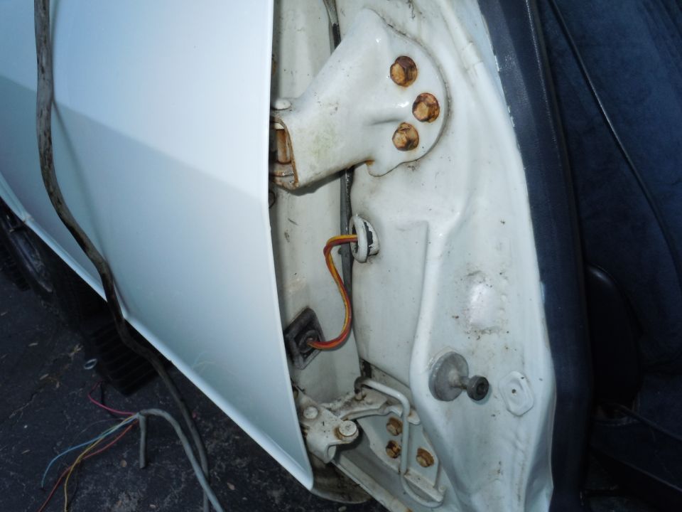 Close-up of a car's door jamb showing the hinge mechanism and some wiring. The paint is white