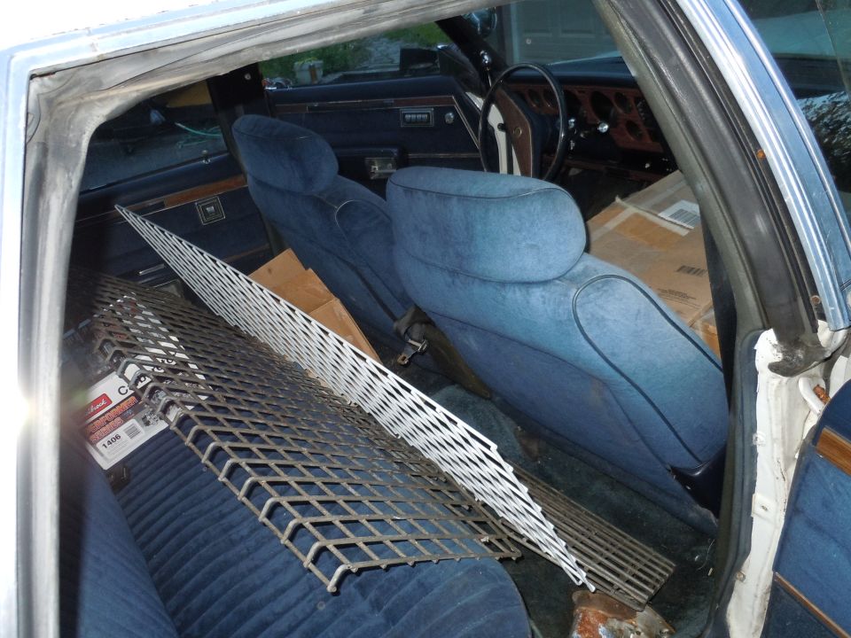 Car interior with blue velour seats, dashboard, steering wheel, and metal grates loaded in the back