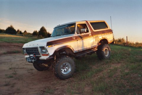 1978 Ford Bronco - This lifted 1978 Ford Bronco, painted in white and brown, is parked on a grassy incline under a clear sky.