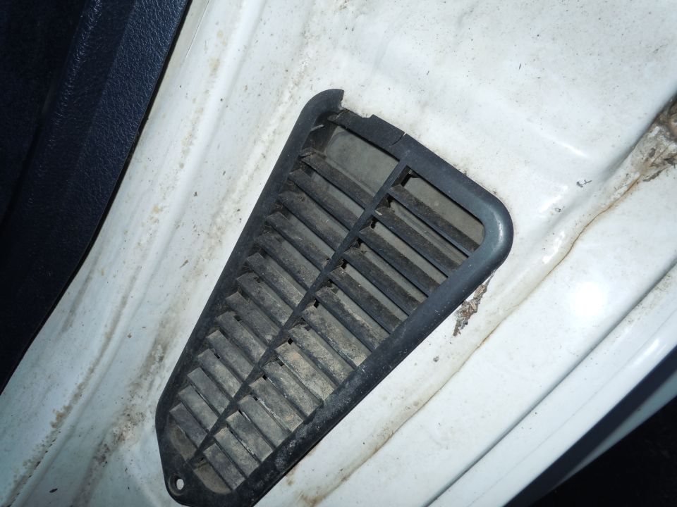 Interior vent on a white car door frame, showing dust and grime