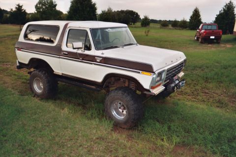 1978 Ford Bronco - A lifted Ford Bronco sits in a grassy field with a red pickup truck parked in the distance.