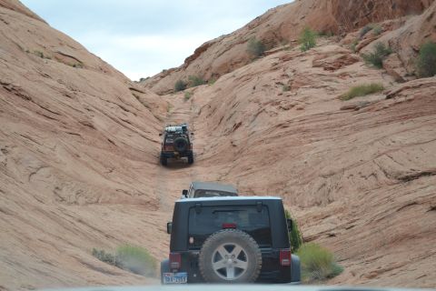 1986 Ford Bronco II - Multiple Jeep Wranglers navigate a narrow dirt path through towering sandstone formations.
