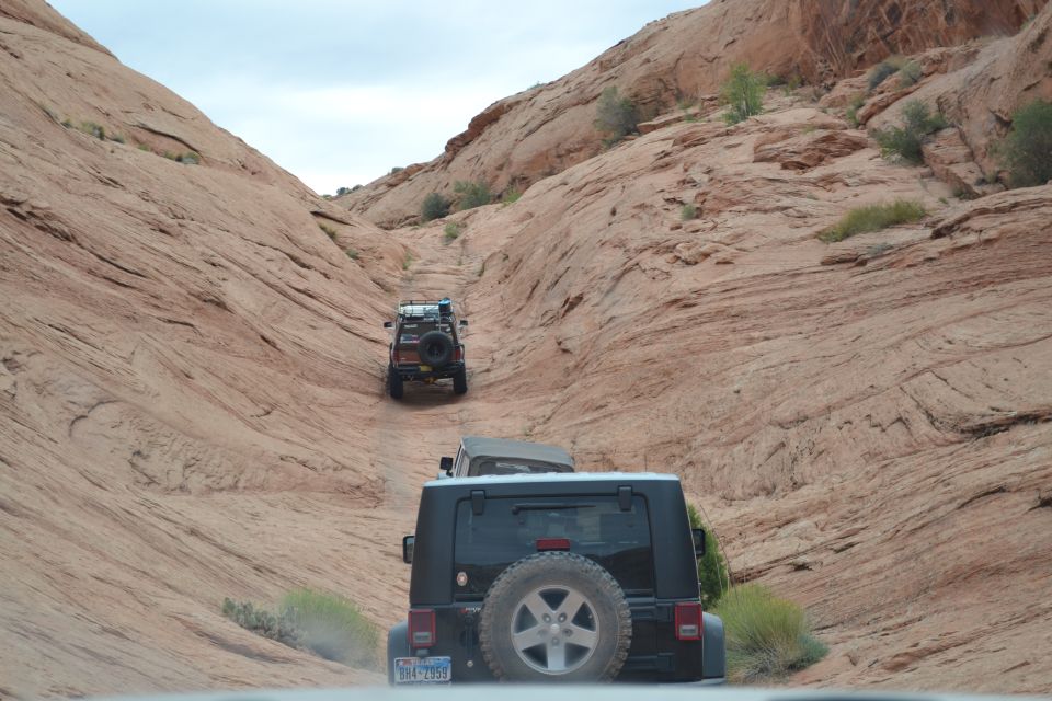 Black Jeep Wrangler rear view, spare tire mounted, driving on dirt road between sandstone cliffs